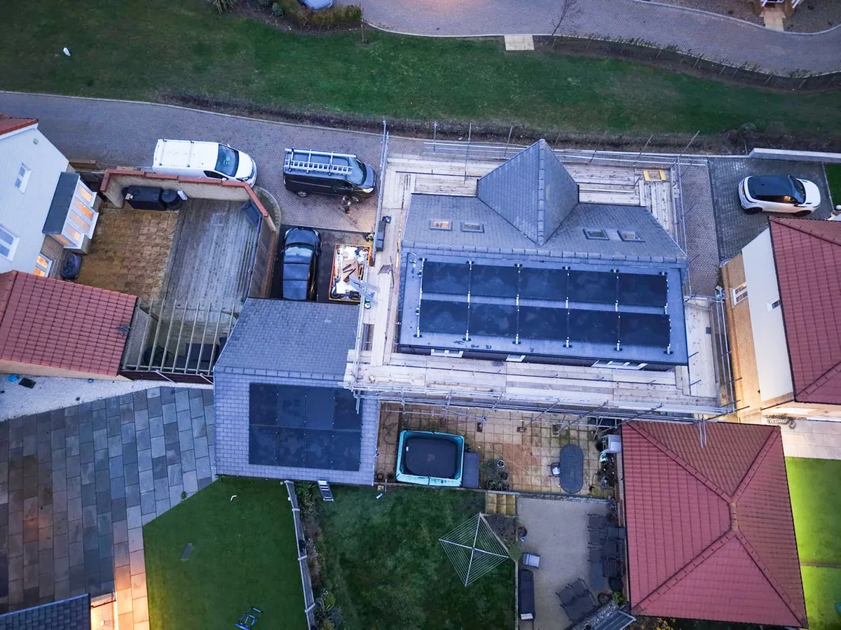 Overhead view of a detached house with a black panel array on the main roof and a second array on the garage roof, scaffolding still up.