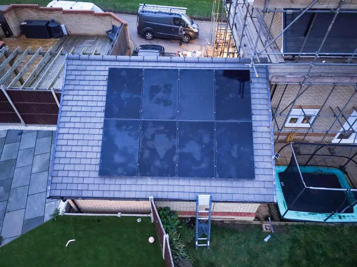 Overhead view of eight black solar panels in two rows of four on a slate garage roof.